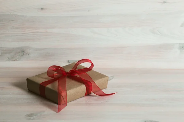 Gift box with red ribbon on a white wooden table.