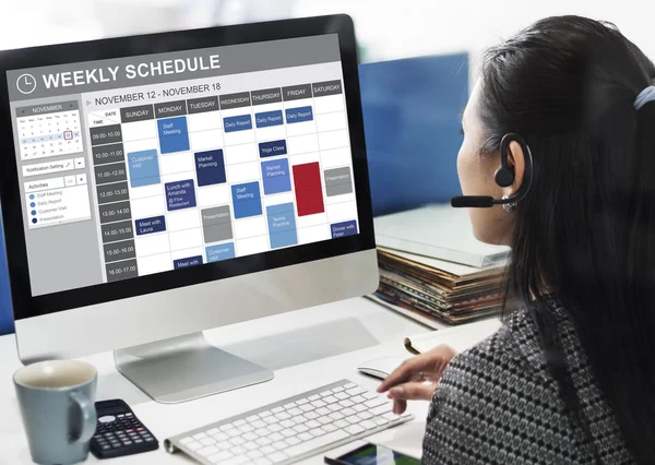 Businesswoman working on computer with weekly schedule
