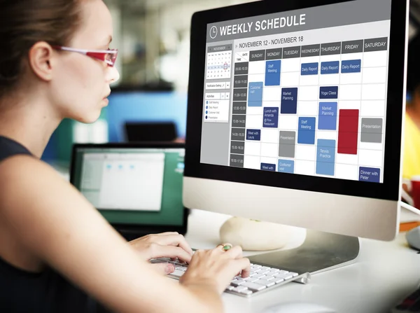 Businesswoman working on computer with weekly schedule