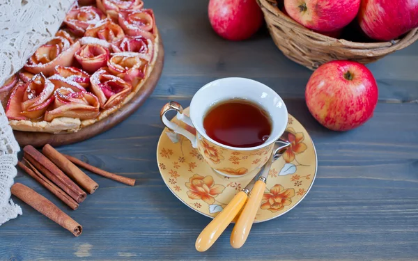 Apple pie, basket with apples and cup of tea on the wooden table