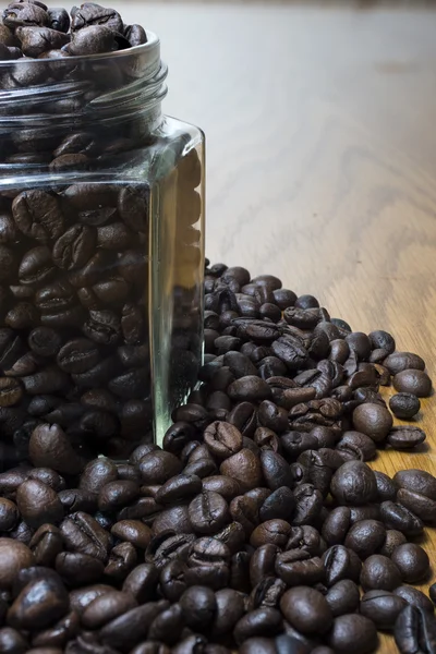 Coffee beans in transparent jar and on wooden table.