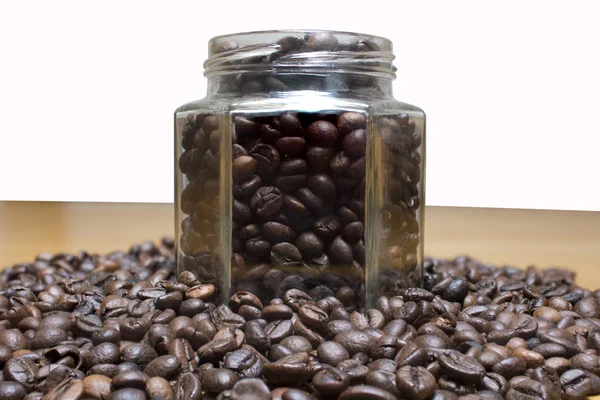 Coffee beans in transparent jar and on wooden table.