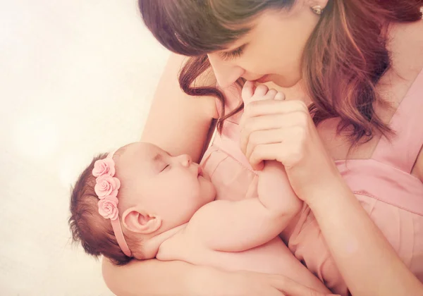 Caring mother kissing fingers of her cute sleeping baby girl