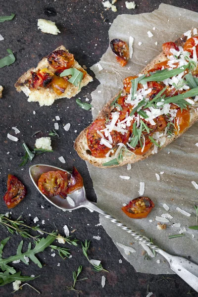 Italian bruschetta with baked cherry tomatoes, parmesan cheese and rocket