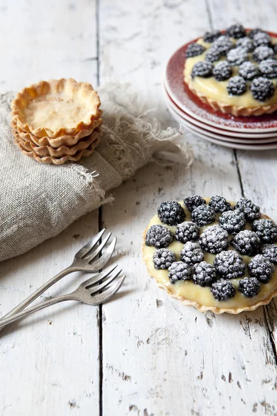 Two homemade blackberries tart with pastry cream on wooden table