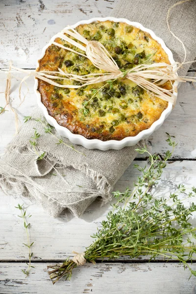 Rustic vegetables french quiche with peas on baking dish on vintage background on wooden table with thyme