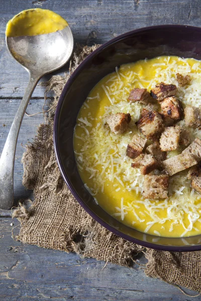 Vegetable soup on bowl with toasted bred croutons and grated parmesan cheese on rustic wooden background with soup spoon