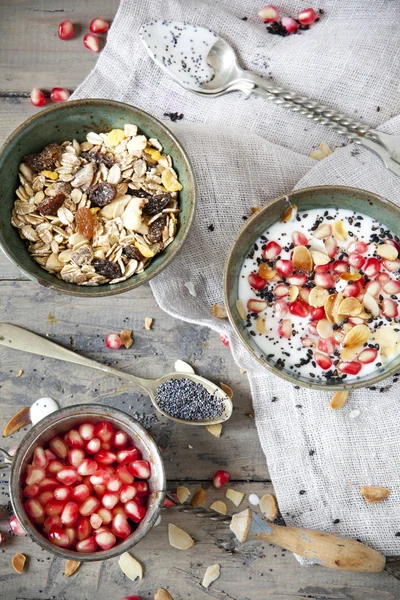 Pomegranate grains on vintage strainer and two bowl of natural yogurt with seed, grains, cereals and muesli with spoon