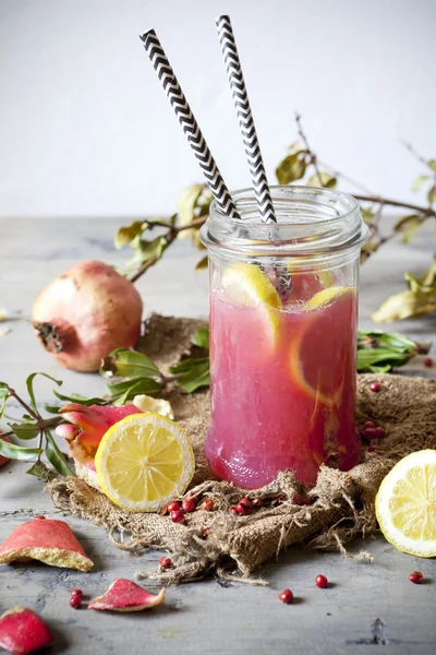 Pomegranate and lemon smoothie on glass jar with two striped straw on rustic background