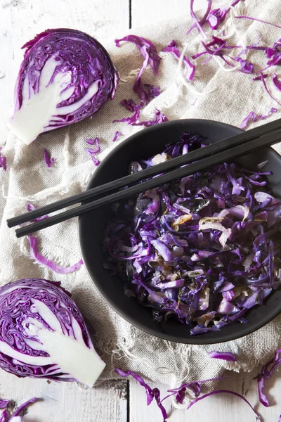 Sauteed purple cabbage on black bowl with japanese chopsticks on white wooden table with napkin