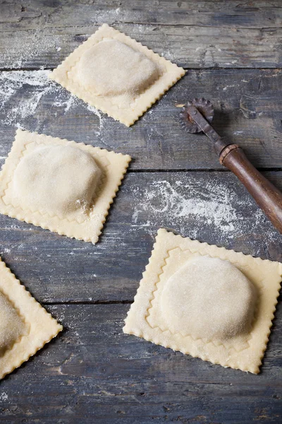 Homemade fresh stuffed ravioli big size on wooden table with flour and wheel cutter
