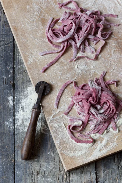 Fresh uncooked homemade pasta tagliatelle with beetroot on chopping board on rustic wooden table