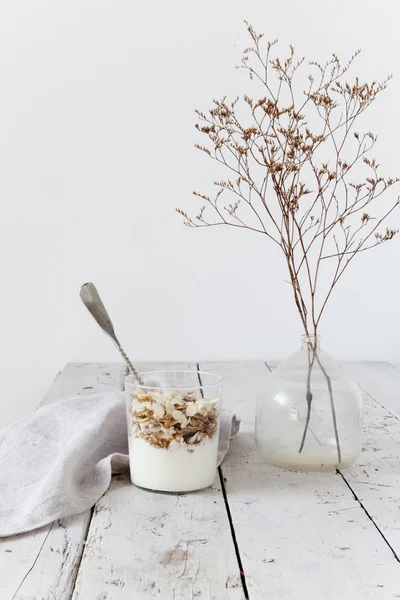 Yogurt and cereals on glass on total white wooden table with dried flowers and spoon