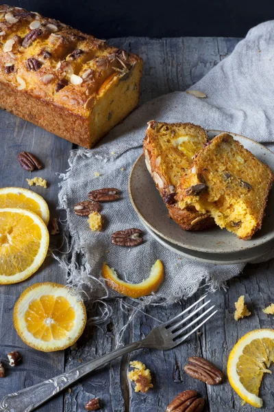 Slices of citrus cake on plate on rustic table with pecan walnuts orange slices and fork