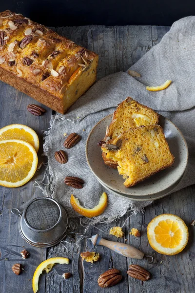 Slices of citrus cake on plate on rustic table with pecan walnuts orange slices and vintage strainer