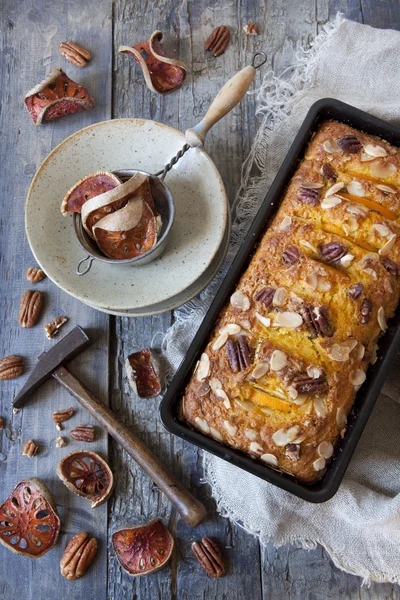 Orange plumcake with pecan walnuts on mold on rustic wooden table with dried orange slices