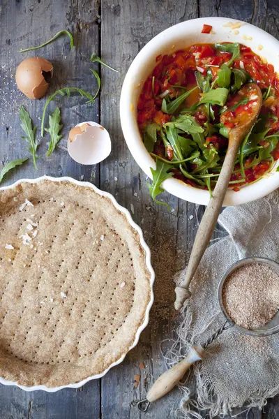 Making a wholemeal quiche with red peppers and rocket on ceramic mold on rustic wooden table with napkin
