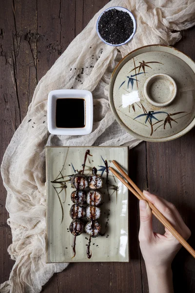 Overhead shot of hands with chopstick taking hosomaki sushi from plate