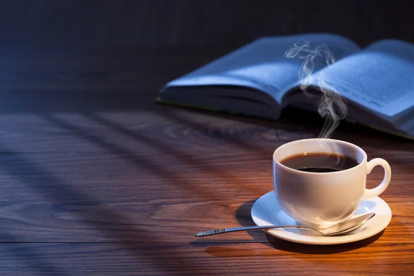 Cup of coffee, open book and glasses on a desk.