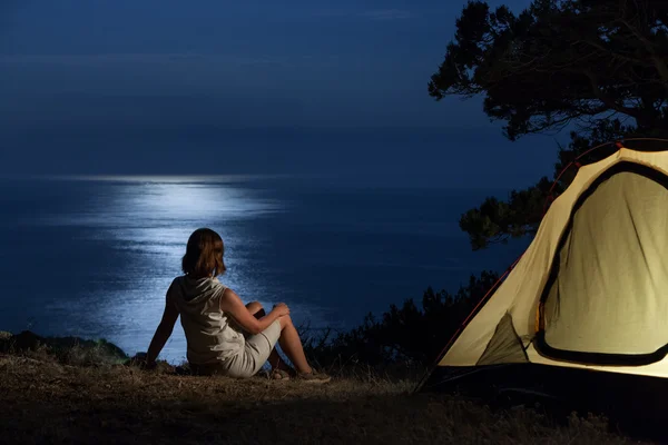 Woman near lit tent at night