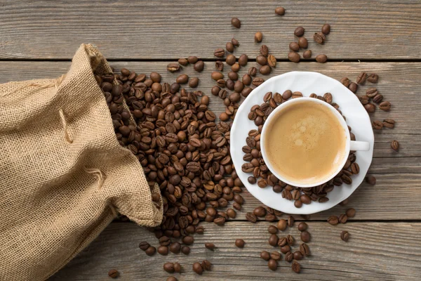 Opened coffee bag with beans and white cup of coffee on a wooden background