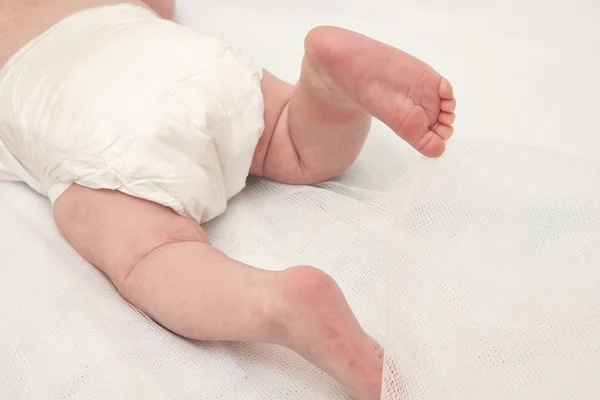 Feet of a two months old baby wearing diapers lying in bed at home