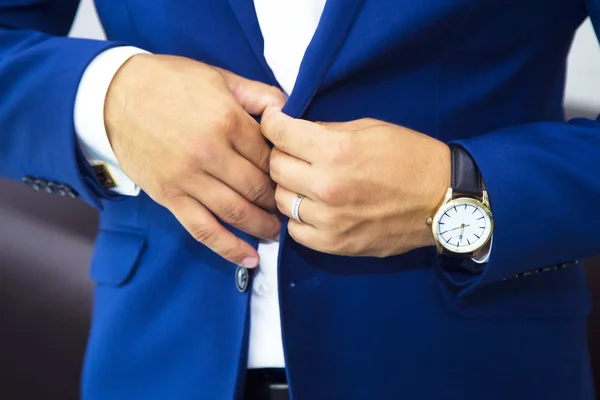 Groom putting on cuff-links as he gets dressed in formal wear