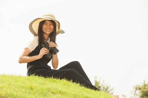 Pretty Asian young  woman sit on mound seeking binoculars .