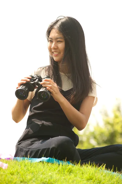 Pretty Asian young  woman sit on mound seeking binoculars .