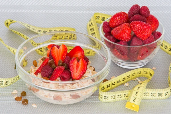 Oatmeal with fresh strawberries and berries with a measuring tape.