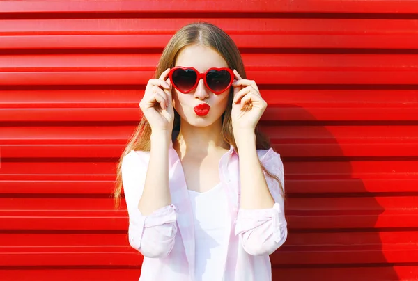 Pretty woman in red sunglasses blowing lips kiss over colorful b