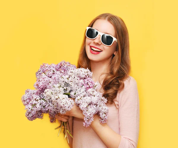 Happy smiling woman with bouquet of lilac flowers over yellow ba