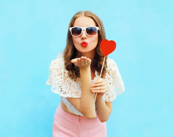 Pretty woman in sunglasses with red heart lollipop sends an air