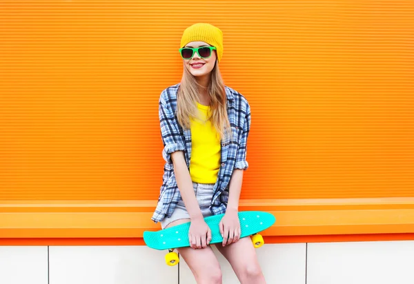 Fashion pretty blonde girl with skateboard in city over colorful