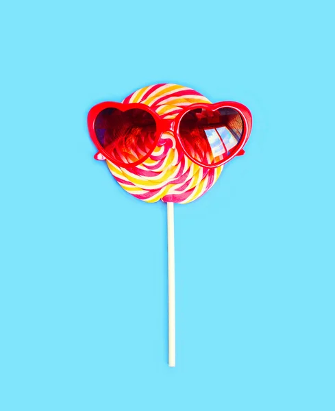Colorful lollipop caramel on stick with sunglasses over blue bac