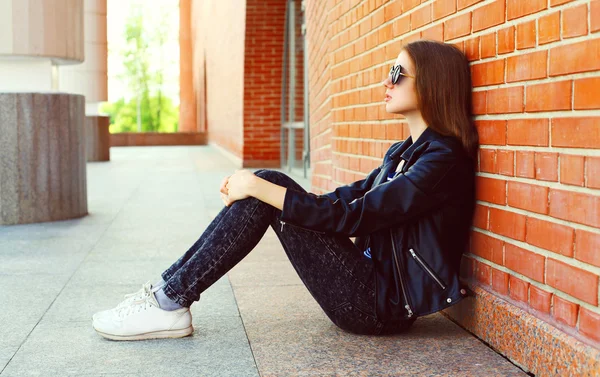 Fashion woman in black rock style sitting over bricks background