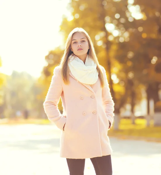 Fashion pretty woman wearing a pink coat in sunny autumn park