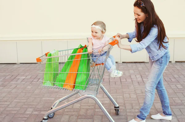 Happy smiling mother and child with trolley cart and colorful sh