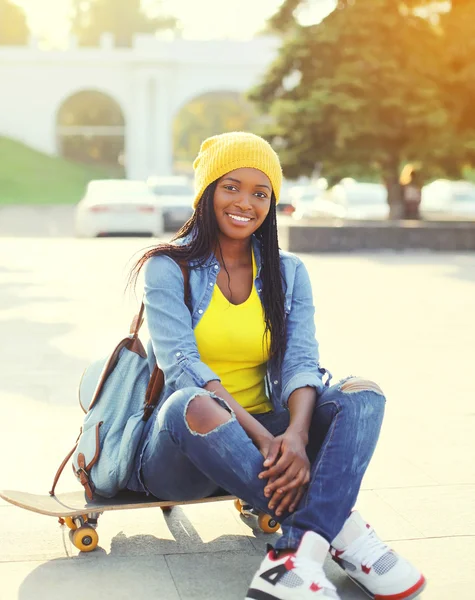 Pretty cool smiling african woman with skateboard in colorful cl