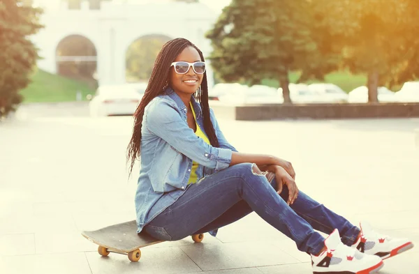 Pretty smiling young african woman with skateboard in city