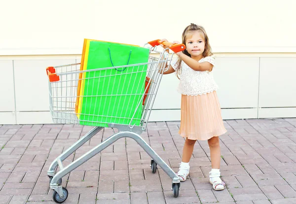Happy little girl child and trolley cart with colorful shopping
