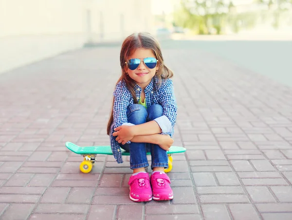 Happy smiling stylish little girl child sitting on skateboard in