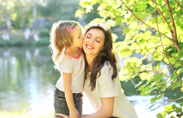 Daughter child kissing happy mother in summer day