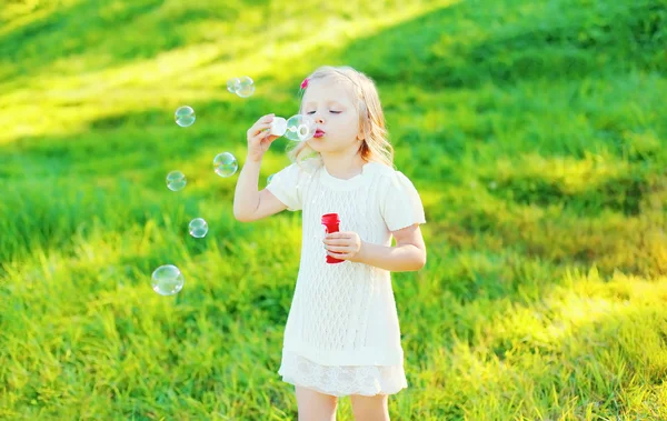 Little girl child blowing soap bubbles in summer day