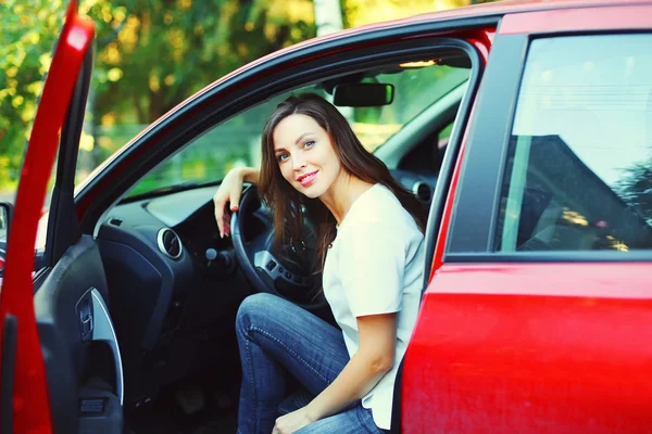 Beautiful smiling young woman driver behind the wheel red car