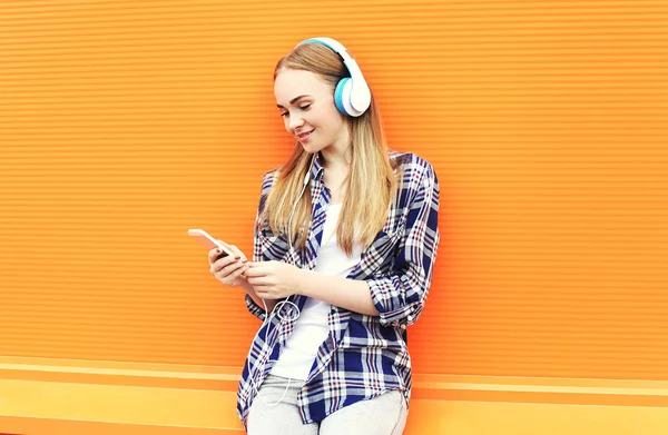Smiling girl in headphones listens to music and using smartphone