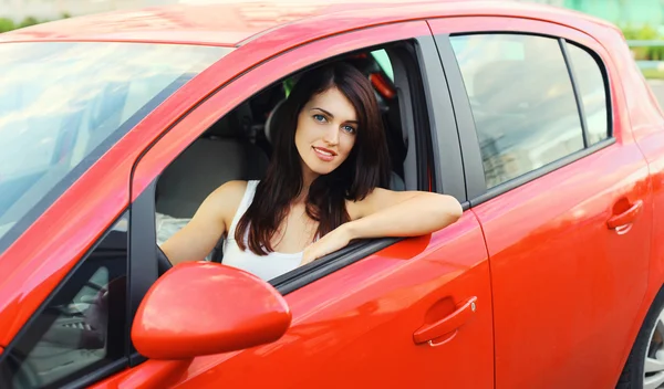 Beautiful young woman driver behind wheel red car