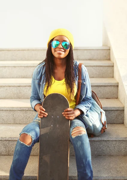 Fashion pretty young african woman with skateboard in colorful c