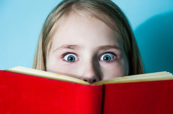 Headshot beautiful little girl hiding behind book, looking scared. Face, facial expressions, emotions, reaction, attitude, attention