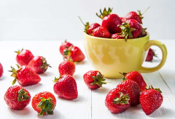 Fresh ripe red strawberries in yellow enamel mug and rough cloth on wooden background